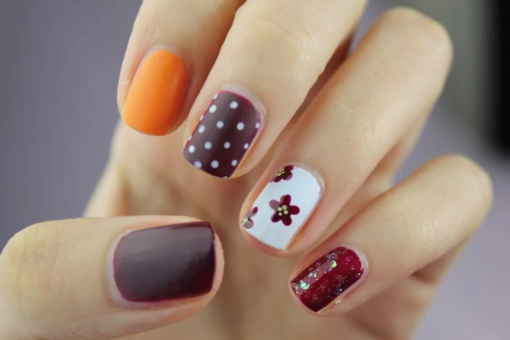 Kurze Nägel mit Punkten und Blumen in Violett und Orange