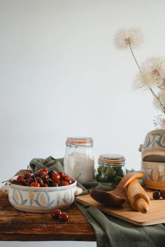 Schale mit Kirschen, Vorratsgläser und Backutensilien auf einem Holztisch