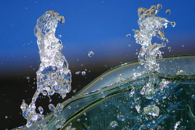 Glas mit spritzendem Wasser auf blauem Hintergrund